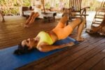 Woman performing workout on mat with resistance band in tranquil outdoor setting.