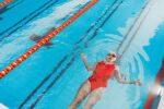 Swimming for Back Pain: Why Doctors Recommend Pool Exercise A woman in a red swimsuit floats on her back in an indoor swimming pool, enjoying a relaxing swim.