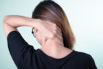 Rear view of a woman massaging her neck, depicting neck pain relief or self-care concepts.