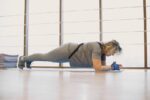 A woman in activewear doing a plank exercise indoors on a yoga mat, promoting fitness and wellness.