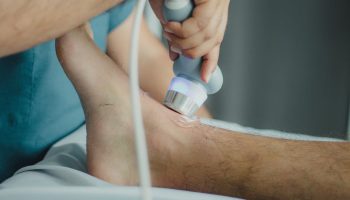 Professional physiotherapist using ultrasound device for leg treatment.