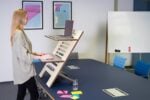 A woman uses an adjustable standing desk in a contemporary Germany office setting.