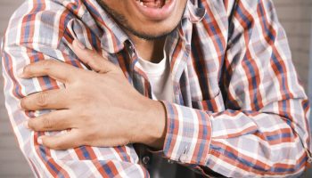 Close-up of a man in plaid shirt experiencing shoulder pain, grasping his arm.