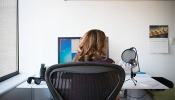 Aeron vs Embody for Back Pain: Which Chair Wins? Adult woman working in a contemporary office setting with computer and microphone.