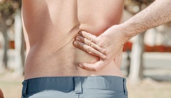 Back Pain Inversion Tables: Do They Actually Work? Close-up of a man holding his lower back in pain, possibly indicating discomfort or injury.